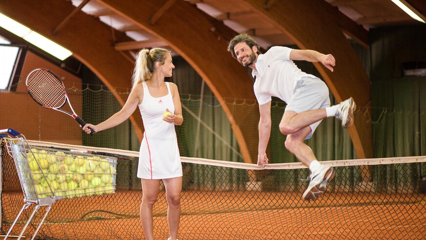 Mann springt über das Tennisnetz zu seiner Tennispartnerin