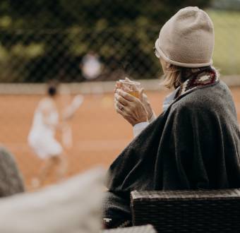 Frau sitzt auf der Terrasse, trinkt Tee und schaut beim Tennis zu