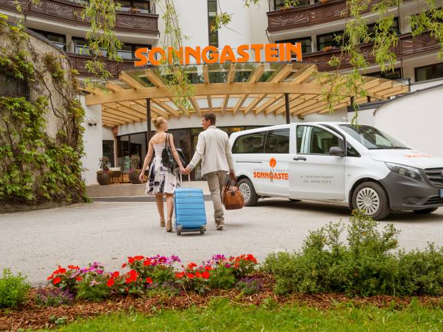 Ein Paar mit Koffer läuft auf den Eingang des Hotel Sonngastein zu