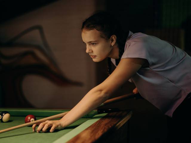 Ein Mädchen schaut gespannt auf den Billardtisch mit dem Billiardqueue in der Hand