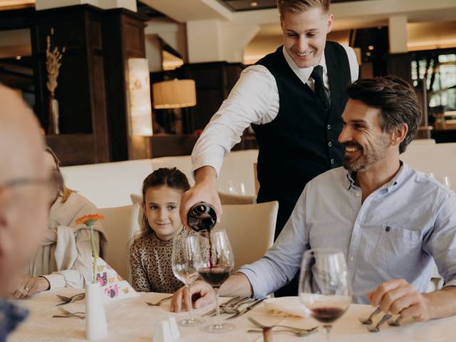 Freundlicher Hotelservice schenkt Rotwein im Restaurant ein – gehobene Gastronomie, Familienessen und persönliche Gastfreundschaft