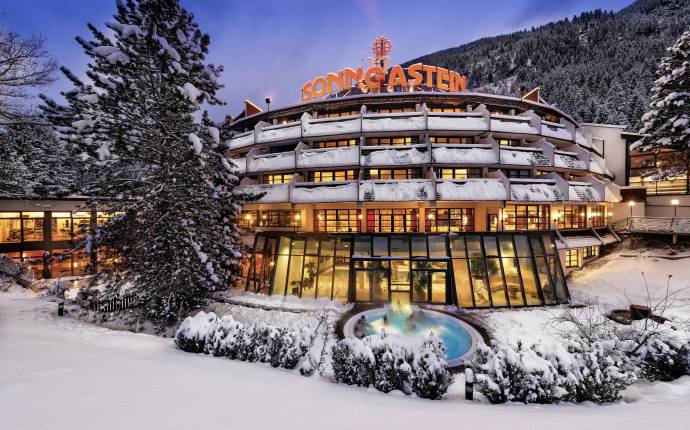 Das Hotel Sonngastein in den verschneiten Alpen mit beleuchtetem Außenpool bei Dämmerung.
