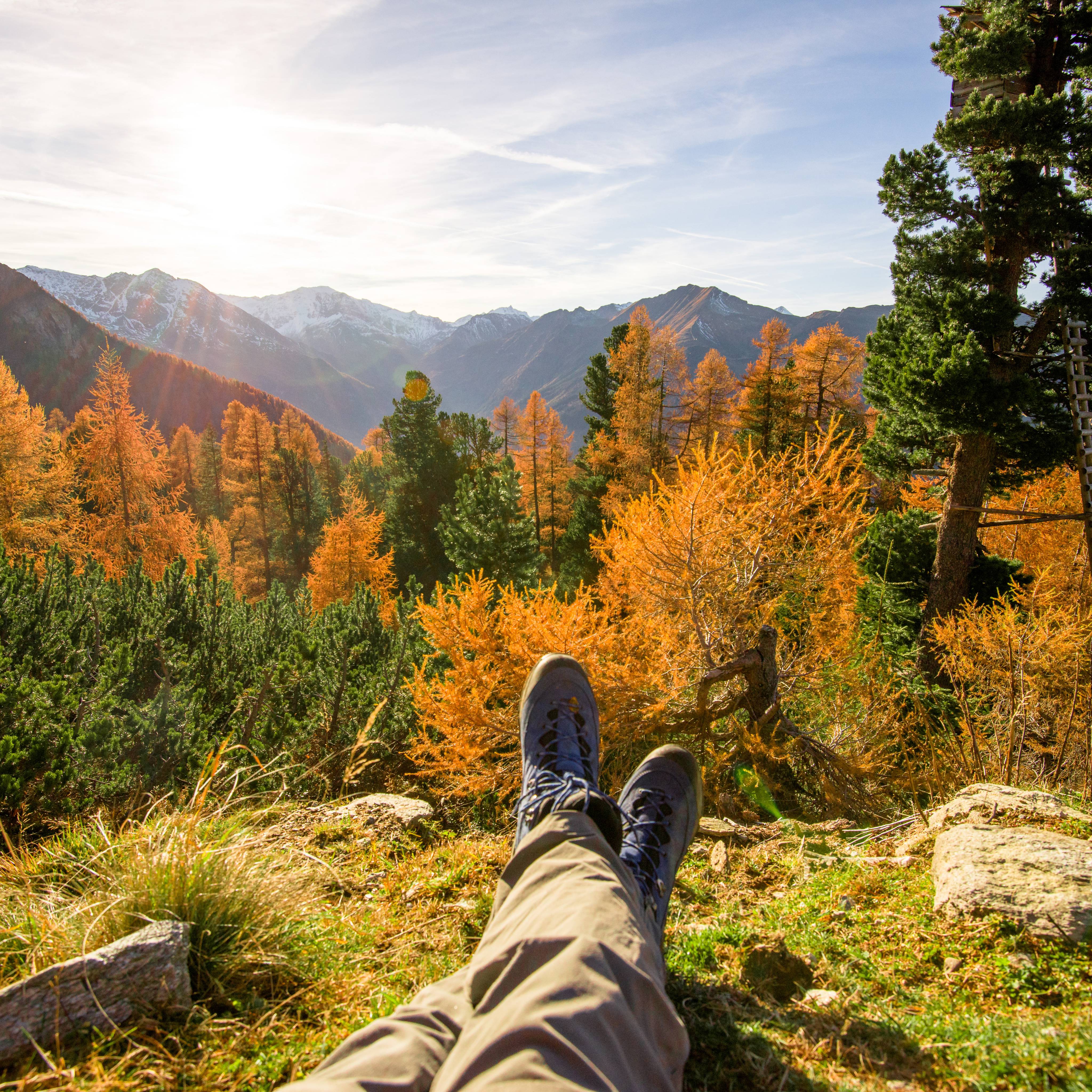 Man sieht die Füße eines Wanderers. er liegt im Gras und vor ihm sieht man die Herbstlichen Wälder und Berge des Gasteinertal