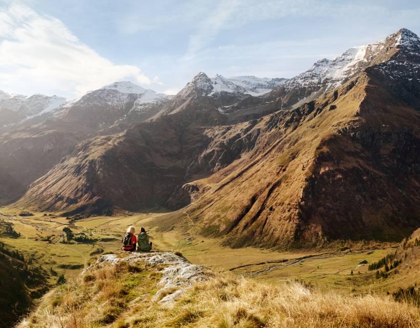 Zwei Menschen sitzen  auf dem Berg, schauen ins Tal und genießen eine Pause der Wanderung