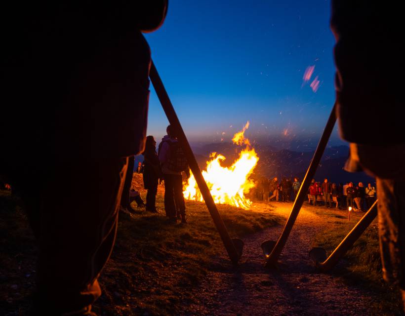 Alphornbläser stehen rund um ein riesiges Lagerfeuer in den Bergen