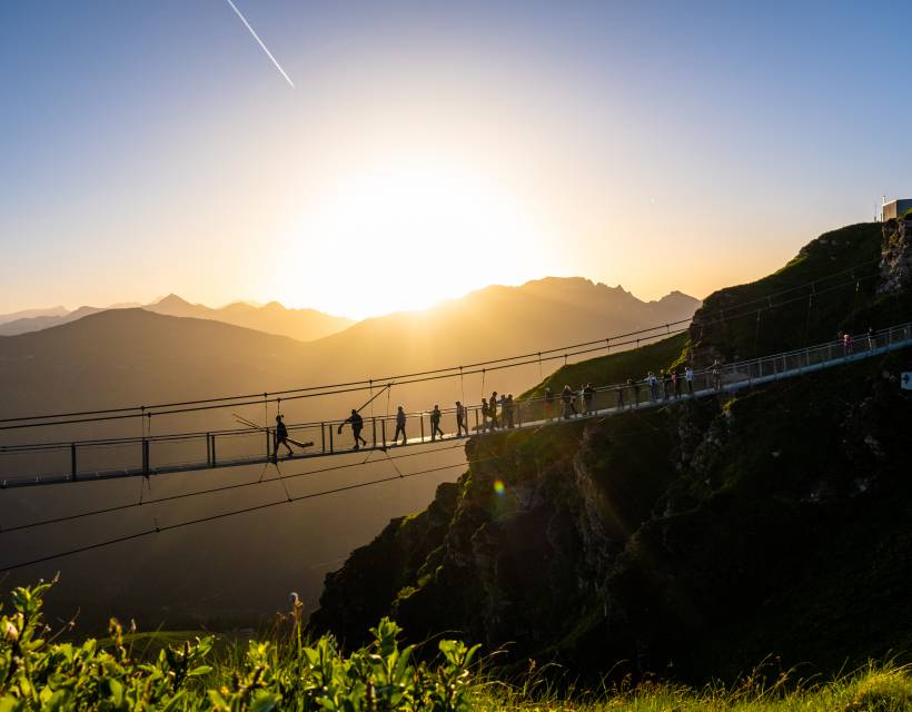 Besucher auf der spektakulären Hängebrücke am Stubnerkogel bei Sonnenuntergang mit Panoramablick über die Alpen im Gasteinertal