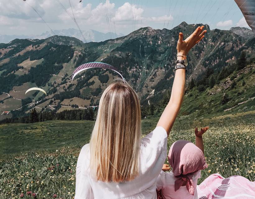 Mutter und Tochter sitze auf einer Picknickdecke und schauen den Paraglidern zu
