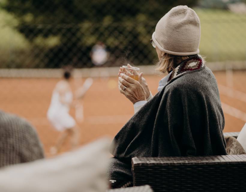 Frau sitzt auf der Terrasse, trinkt Tee und schaut beim Tennis zu