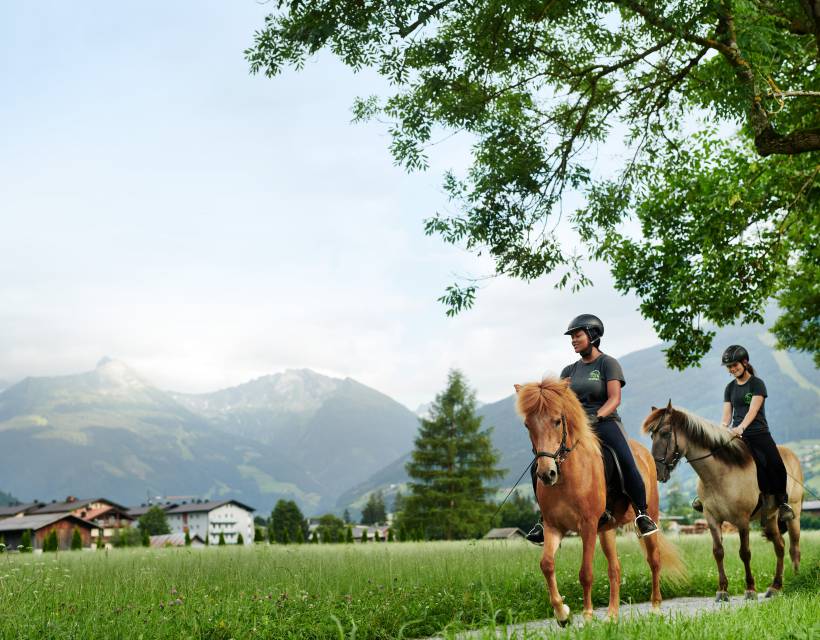 Zwei Reiterinnen auf ihren Pferden reiten entlang des Ortsrandes von Gastein