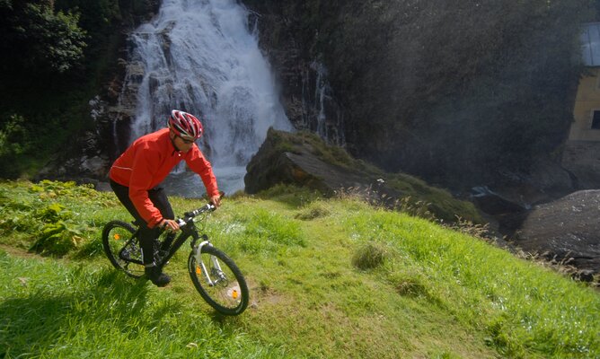 Mann beim Mountainbiken vor einem Wasserfall