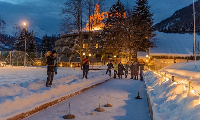 Gäste beim Flutlicht-Eisstockschießen am Abend mit Blick aufs Hotel